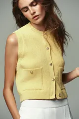 Chaleco amarillo de punto con cuello redondo y sisas amplias. Tiene cierre frontal con botones dorados y dos bolsillos de parche con botón.
