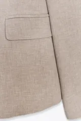 Blazer color beige de corte entallado, con cuello solapa y mangas largas. Tiene bolsillos con solapa en la parte delantera y cierre cruzado con botones.