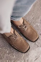 Mocasín de cuero negro con cordones y tachas metálicas en la puntera.