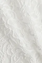 Top sin mangas color blanco, de tejido transparente con diseño bordado tono sobre tono en nudo francés. Modelo con cuello redondo y cierre oculto con cierre de corchete atrás.