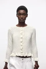 Chaqueta de punto amarilla con cuello redondo, manga larga y cierre frontal con botones. Detalle de volantes en los bordes.