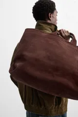 Bolso tipo shopper marrón de piel con acabado serraje. Tiene dos asas de mano y un bolsillo interior con cierre.