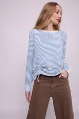Remera de mangas largas a rayas horizontales celestes y blancas, con cuello redondo y frunce lateral con cordón ajustable.