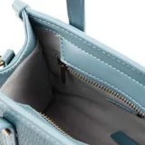 Cartera tote mini color celeste de cuero sintético con textura granulada. Tiene doble asa corta, correa larga regulable y extraíble, cierre superior y herrajes plateados. El frente está adornado con el logo metálico de la marca.
