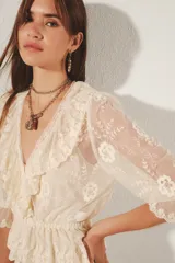 Blusa de encaje color crema con bordados florales, escote en V profundo con volados y mangas 3/4 terminadas en volantes. Diseño de estilo romántico con transparencias y cintura elástica.