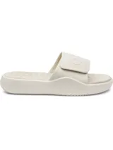 Sandalia tipo slide para hombre, color blanco hueso o crema, con tira ancha ajustable mediante velcro. La tira presenta un logo en relieve. La plantilla es texturizada para mayor confort y la suela es gruesa.