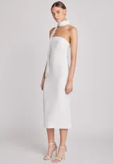 Vestido midi blanco de corte recto, con escote asimétrico y cuello halter. Incluye una cinta ancha que rodea el cuello y cae sobre el hombro.