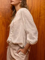 Blusa color crema de gasa bordada, con escote en V, abertura central con botones y mangas largas con puño.