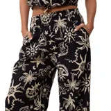 Pantalón de tela negro con estampado de palmeras, soles y estrellas de mar en color beige.