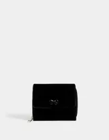 Billetera pequeña de cuerina color negro con cierre de cremallera y broche. Presenta un moño metálico en el frente.