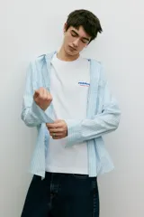 Remera blanca de algodón con cuello redondo y estampado pequeño en el pecho con el texto "Peanuts Racing Team" en color azul.