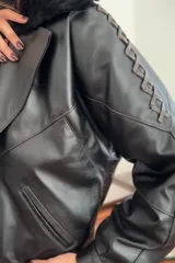 Campera bomber negra de cuero con cuello de piel sintética negra, forro interior y detalles de pasamanería en cuero marrón gastado en las mangas.