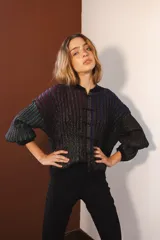 Cárdigan tejido con lurex, con cuello redondo, manga 3/4 y cierre frontal con botones forrados. Diseño con rayas verticales en tonos verde, azul y violeta sobre fondo negro con brillo.