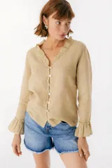 Blusa blanca de lino con botones de nácar, volados en el escote y mangas largas con puños acampanados. Corte recto y holgado.