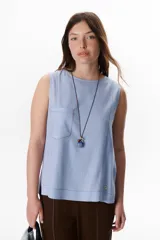 Top sin mangas color terracota con cuello redondo y bolsillo frontal. Presenta costuras a contratono en blanco que definen los bordes y el bolsillo.