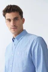 Camisa oxford celeste con rayas verticales blancas, de manga larga y corte regular. Tiene cuello abotonado, bolsillo en el pecho y logo bordado.