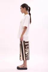 Remera blanca de algodón, corte oversize, con cuello redondo y manga corta. Presenta un estampado frontal con varias reposeras y hamacas de playa, y el texto "LA SIESTA".