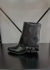 Botas de cuero sintético negras, de caña media y punta fina. Presentan una correa con hebilla metálica plateada alrededor del tobillo.