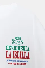 Camiseta blanca de algodón con cuello redondo y estampado frontal con el logo de la cevichería "La Islilla" en verde y rojo.