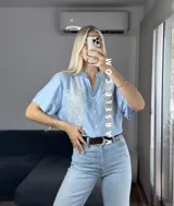 Camisa celeste de manga corta con bordado floral blanco en el frente. Tiene cuello mao y cierre frontal con botones.