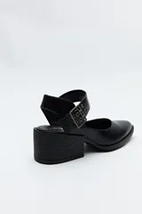 Zapato negro tipo zueco con acabado charol, tira ancha con hebilla metálica y taco ancho de altura media.