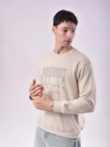 Buzo color beige claro con cuello redondo y puños y cintura acanalados. Estampado frontal con texto en color gris.