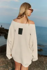 Sweater tejido color crema con cuello amplio que deja un hombro al descubierto. Presenta un estampado con dibujos de estilo boceto en negro y rojo, y detalles de roturas en las mangas.