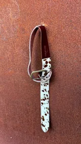 Cinturón de cuero blanco con estampado de manchas marrones, hebilla metálica dorada y reverso de cuero color borgoña.