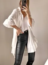 Camisa blanca de tejido suave tipo seda, con mangas tres cuartos y volados irregulares en mangas y ruedo. Tiene un largo ligeramente mayor en la espalda.