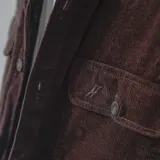 Campera negra de pana con cuello camisero, cierre frontal con botones a presión, dos bolsillos de parche en el pecho y corte recto.