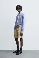 Bermuda color beige confeccionada en tejido de algodón y lino, con corte relaxed fit, cintura ajustable con cinturón de la misma tela, pliegues frontales, bolsillos delanteros y traseros, cierre frontal con cremallera y botón.