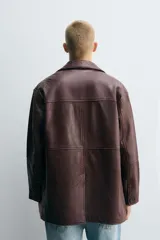 Cazadora de hombre de corte relajado, confeccionada en piel con textura irregular color marrón oscuro (vino/borgoña). Presenta cuello solapa, manga larga con puño abotonado, bolsillos de vivo en cadera, bolsillo interior y cierre frontal con botonadura.