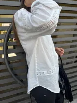 Camisa blanca de mangas largas con detalles de encaje en el frente, cuello y puños.