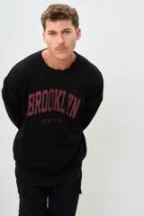 Buzo negro de corte holgado con estampa frontal de letras en color borgoña que dice "BROOKLYN" y "NEW YORK".