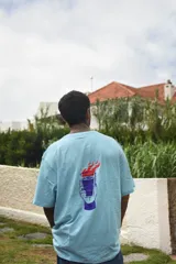 Remera color arena de corte recto y mangas cortas, con cuello redondo y estampado pequeño en el pecho con una carita sonriente y la palabra "Tuya.".