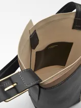 Bolso tipo tote de cuero negro con detalles en beige y correa larga ajustable con hebilla metálica.
