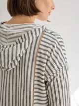 Chomba a rayas horizontales color crudo y gris, con capucha y botones de madera. Tiene cordones de ajuste en la capucha y puños con ribete verde flúor.