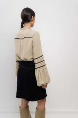 Camisa beige de lino con cuello mao, cierre frontal con botones y detalles de puntilla negra en mangas y frente.