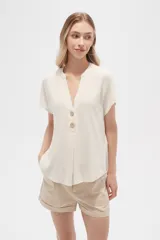 Blusa color crudo de viscosa, corte holgado, con cuello en v y cierre frontal con dos botones de madera.