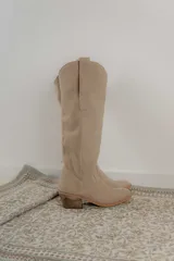 Bota alta de cuero color beige, estilo texana, con caña alta y taco bajo.