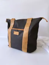 Bolso tipo tote de lona color fucsia con asas de cuero marrón, bolsillo interno y externo.