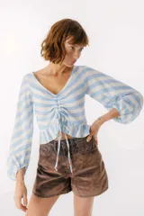 Blusa blanca de lino con escote en V, mangas largas abullonadas y frunce central.