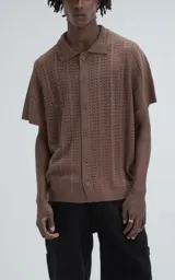 Camisa de tejido de punto color café, manga corta y cuello polo con botones frontales. Presenta un patrón calado de espiga o chevron.