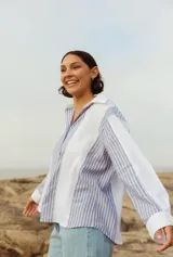 Camisa de lino a rayas verticales azules y blancas, con cuello clásico y mangas largas con puños abotonados. Corte recto y holgado.