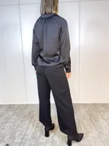 Camisa negra de satén plisado, con cuello camisero, mangas largas con puños abotonados y cierre frontal con botones.