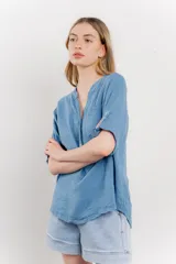 Camisa azul de lino con escote en V abotonado, bolsillo frontal y mangas 3/4 con trabilla.