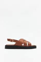 Sandalias de símil cuero color marrón con tiras cruzadas en el empeine, ajuste con hebilla en el tobillo y plataforma baja color negro.