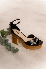 Sandalias de cuero color marrón con plataforma de madera y taco cuadrado. Tiras cruzadas en el empeine y pulsera al tobillo con hebilla dorada.