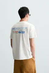 Camiseta blanca de corte recto, cuello redondo y manga corta. Estampado pequeño en el frente y estampado grande en la espalda con texto en color rojo.