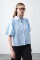 Camisa de algodón celeste claro, con cuello camisero y mangas cortas abullonadas. Presenta un corte relajado y cierre frontal de botones.